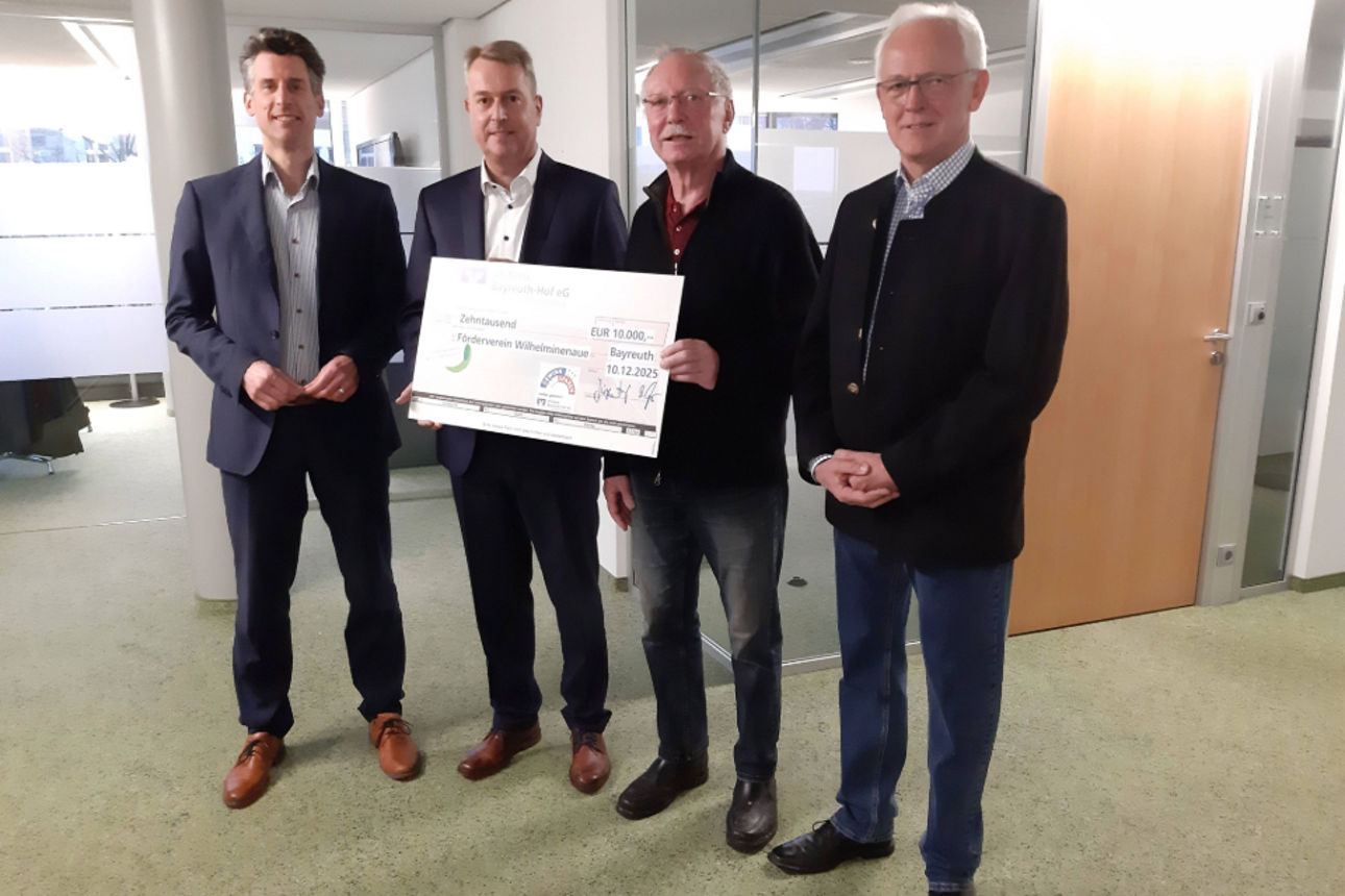 Vier Personen stehen in einem Büro und halten gemeinsam einen großen Spendenscheck