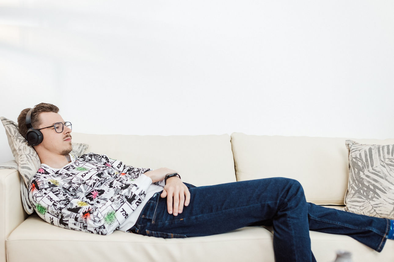 Junger Mann mit aufgesetzten Kopfhörern liegt entspannt auf einer Couch.