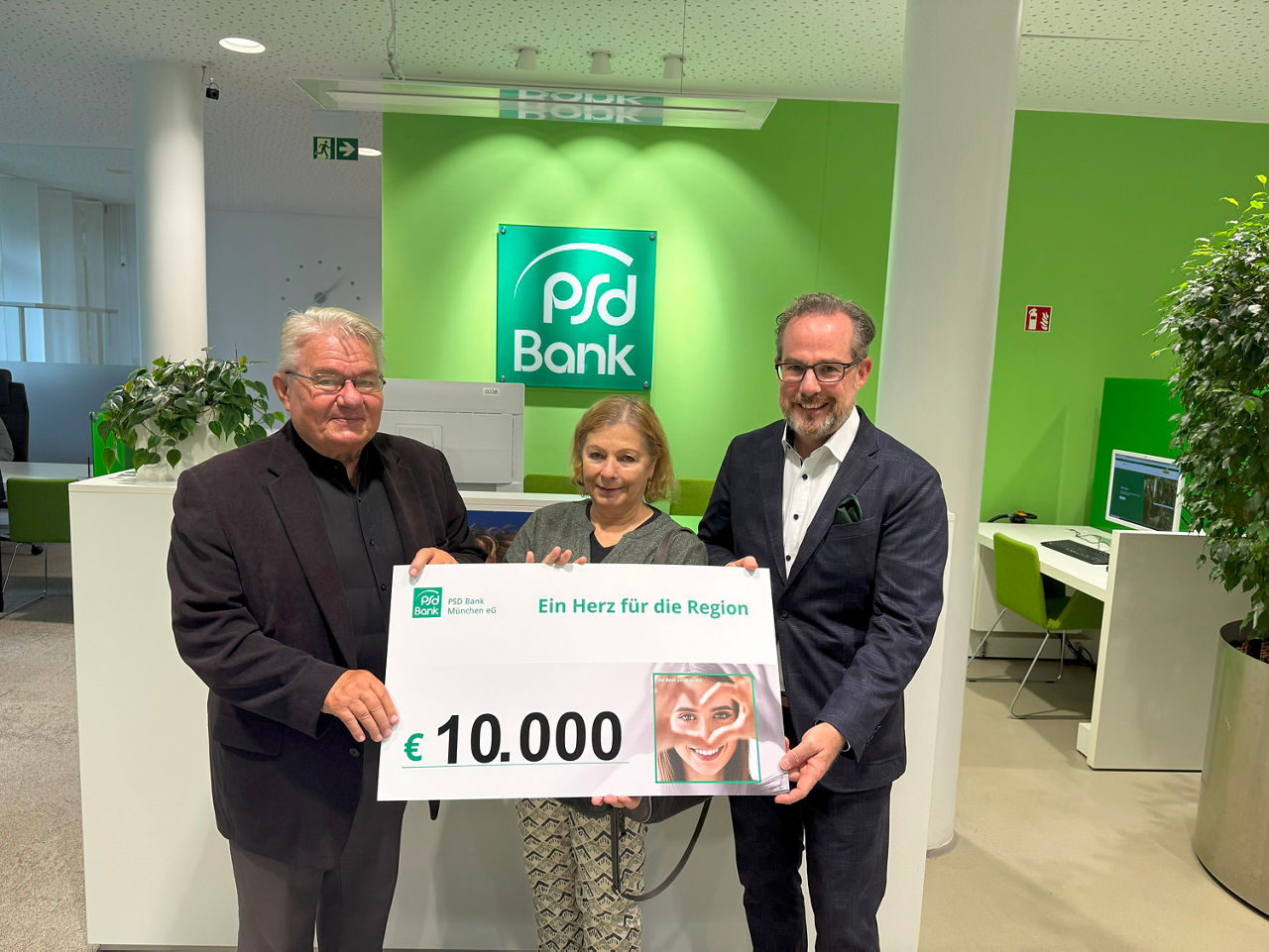 Zwei Männer und eine Frau stehen nebeneinander in der Filiale der PSD Bank. Zusammen halten sie einen Scheck in Höhe von 10.000 Euro in der Hand.