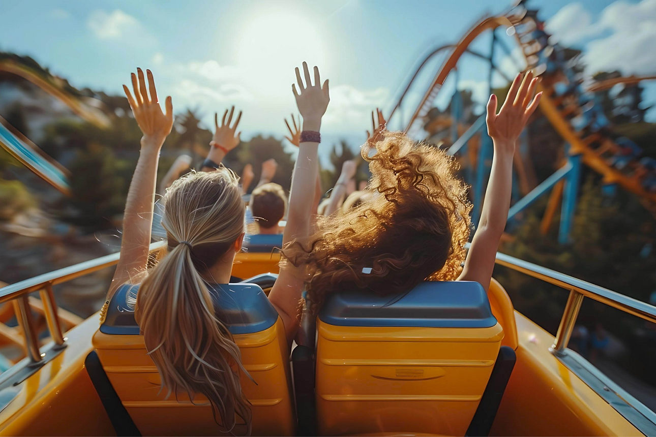 Personen fahren Achterbahn mit erhobenen Händen, actionreiche Freizeitparkszene bei Sonnenschein