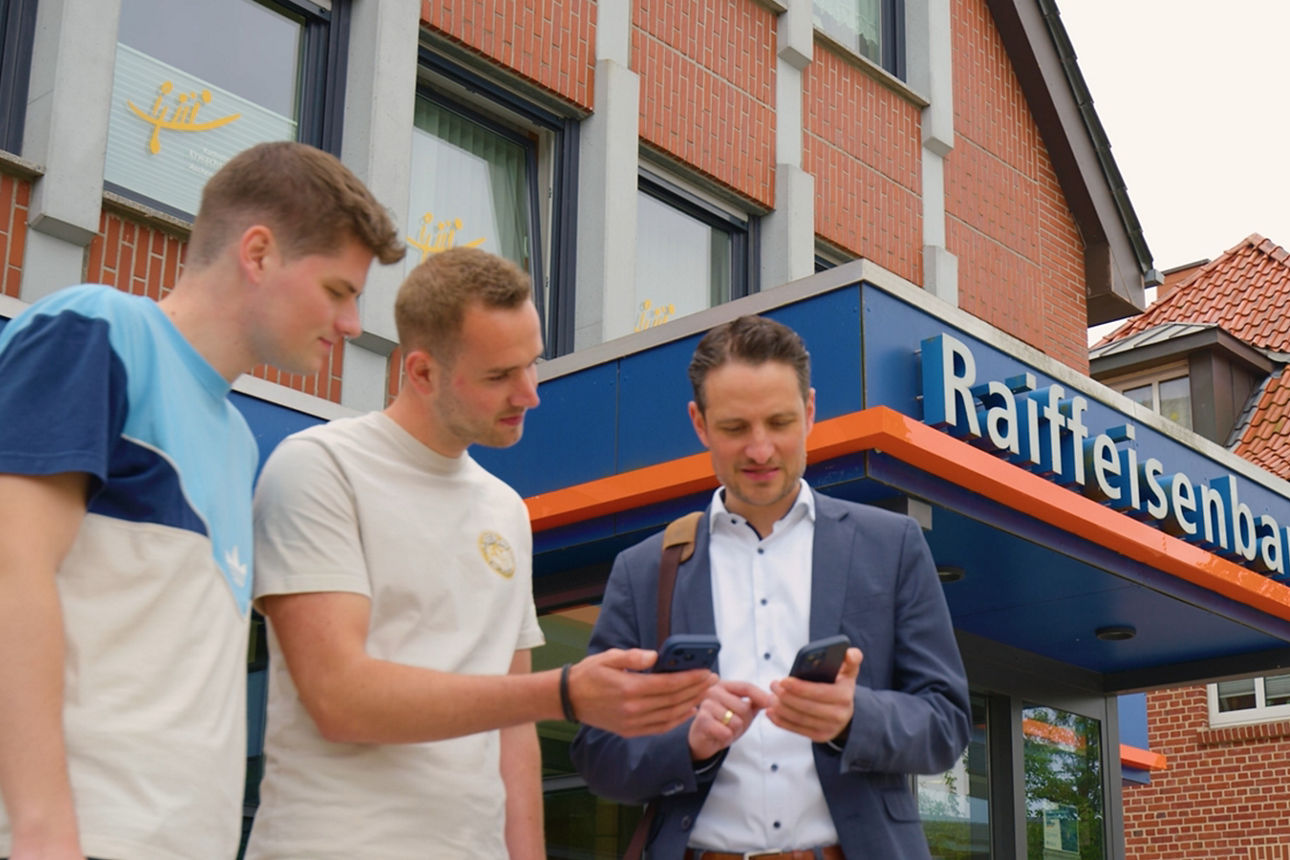 3 Personen, die vor einer Bank auf ihr Handy schauen