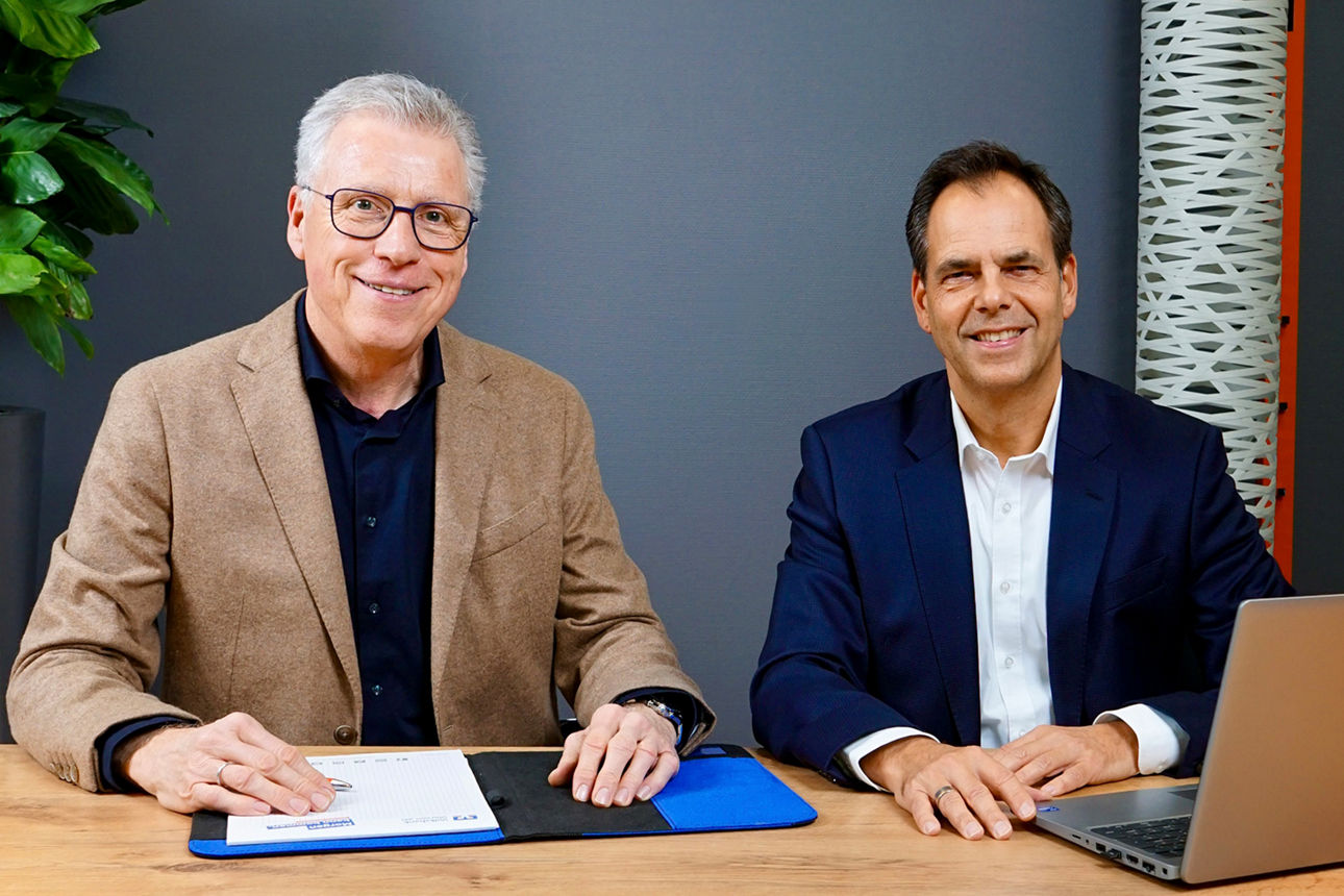 2 Männer sitzen an einem Tisch vor ihren Unterlagen