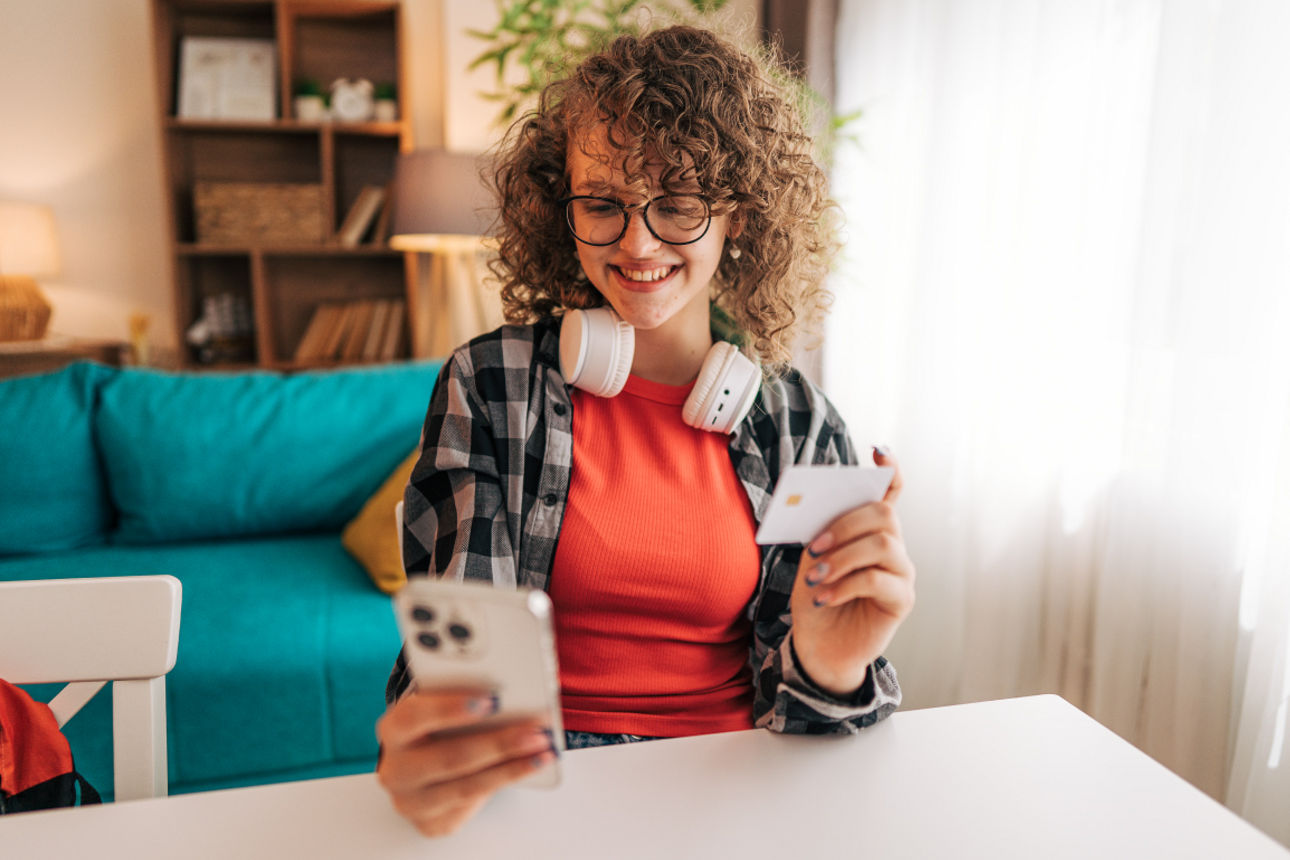 Lächelnder Teenager, der zu Hause online mit Smartphone und Kreditkarte bezahlt