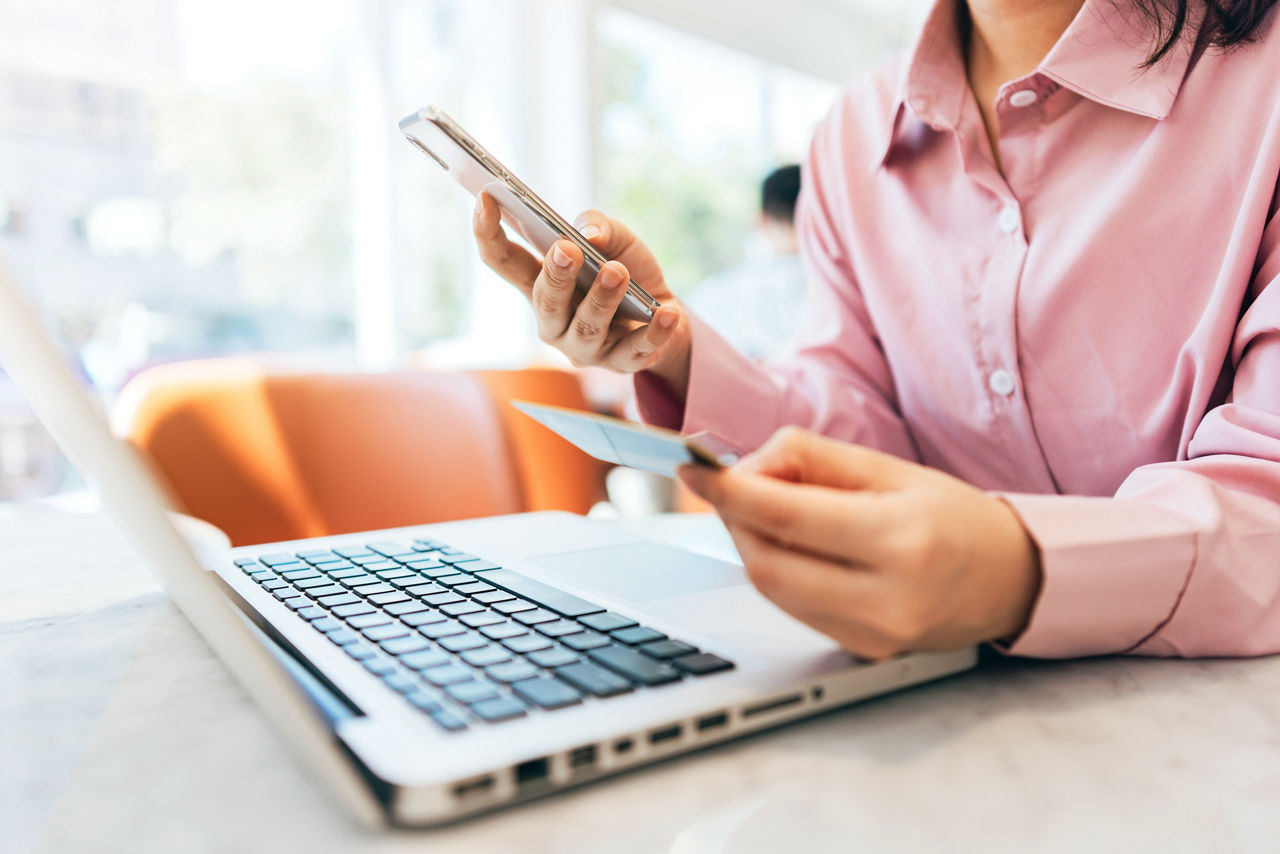 Frau am Laptop mit Handy und Bankkarte in der Hand