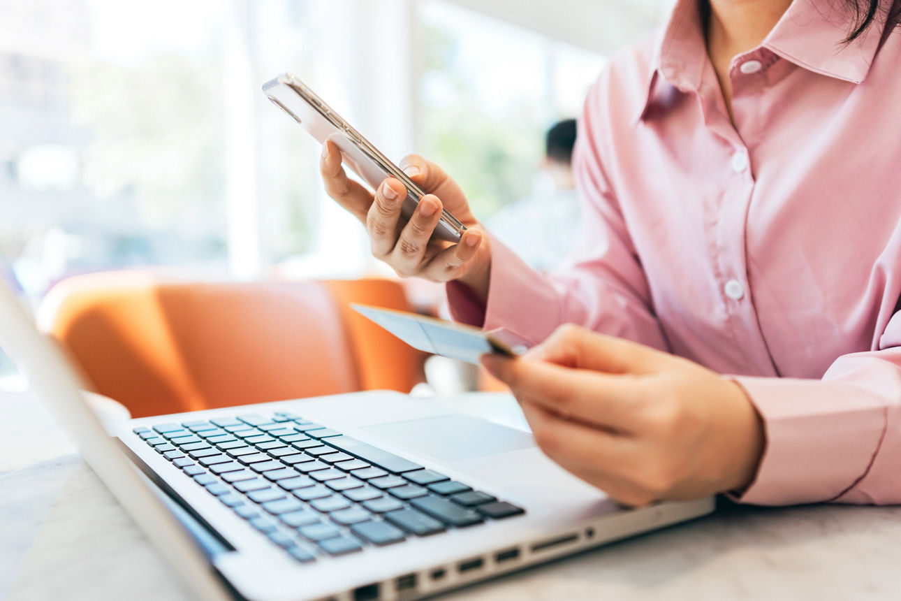 Eine Frau sitzt mkit Bankkarte und Handy vor ihrem Laptop