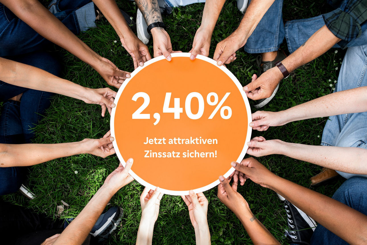 Viele Hände halten ein rundes Schild auf dem der Zinssatz für den Mitgliedersparbrief abgebildet ist