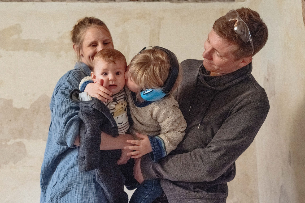 Eltern mit zwei Kindern stehen in einem renovierungsbedürftigen Haus.