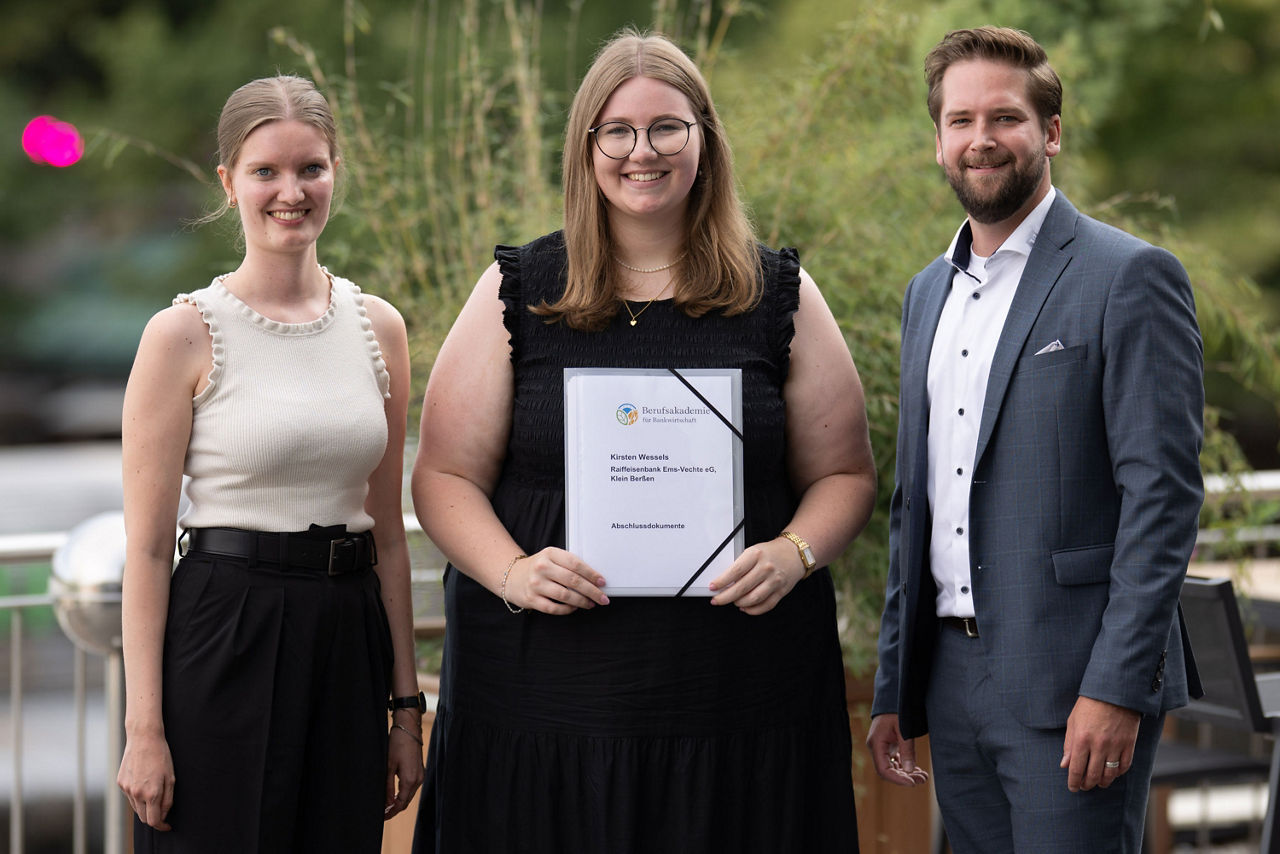 Kirsten Wessels präsentiert ihr Abschlusszeugnis vom dualen Studium, neben ihr stehen Maren Overkamp und Christian König