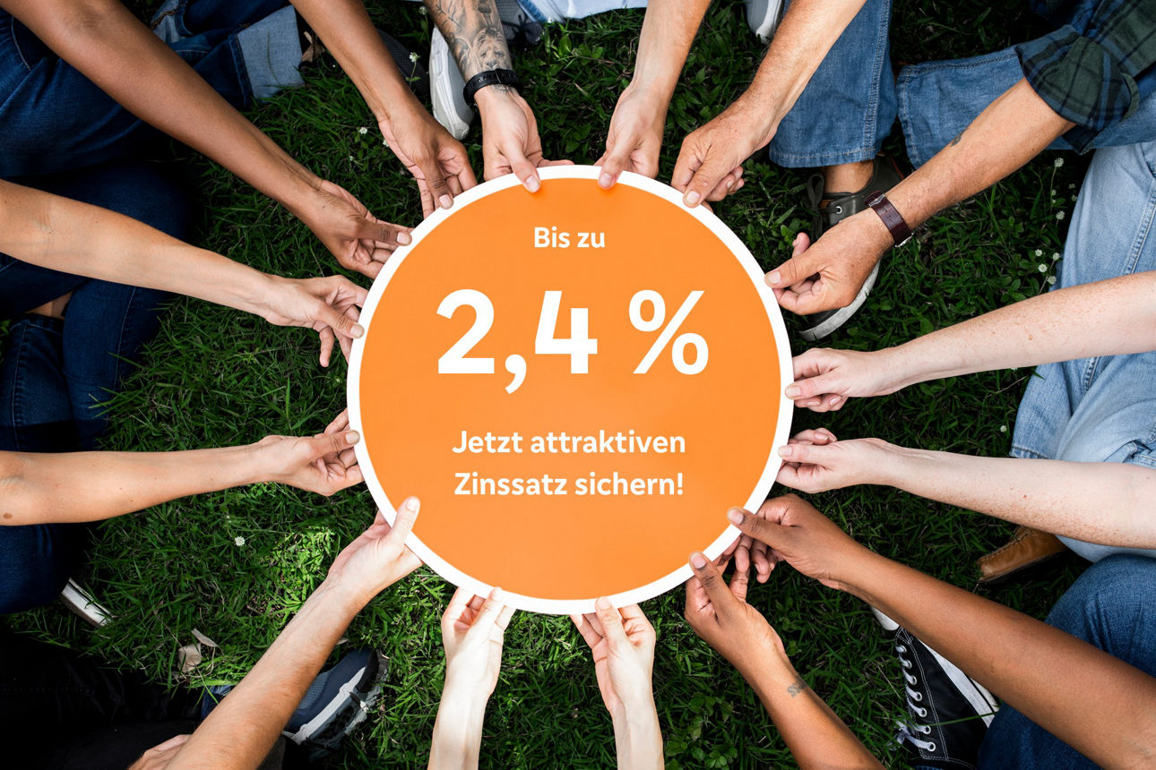 Viele Hände halten ein rundes Schild auf dem der Zinssatz für den Mitgliedersparbrief abgebildet ist