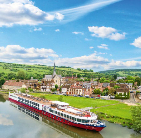 Ein Kreuzfahrtschiff auf der Seine, im Hintergrund schöne Häuser und ein blauer Himmel mit Wolken.