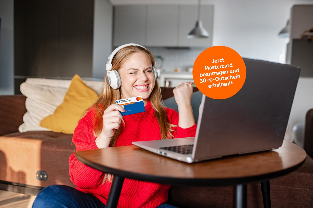 Eine Frau sitzt jubelnd mit Ihrer Mastercard in der Hand vor Ihrem Notebook.