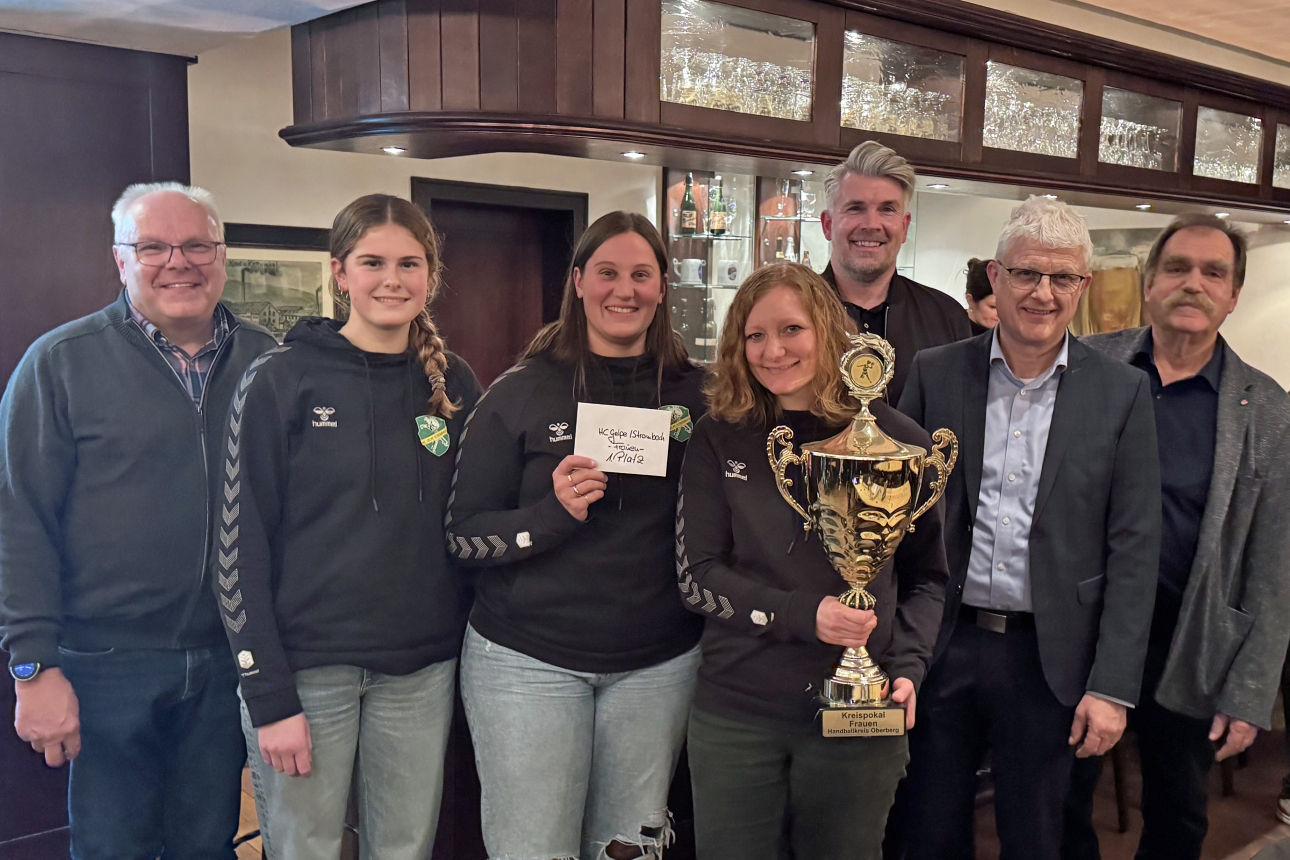Gruppenfoto bei der Pokalübergabe: Niederlassungsleiter Michael Eiteneuer überreicht den Volksbank-Oberberg-Pokal an Spielerinnen der HC Gelpe/Strombach, die den Pokal in den Händen halten. Mehrere Beteiligte stehen gemeinsam in einem Innenraum.
