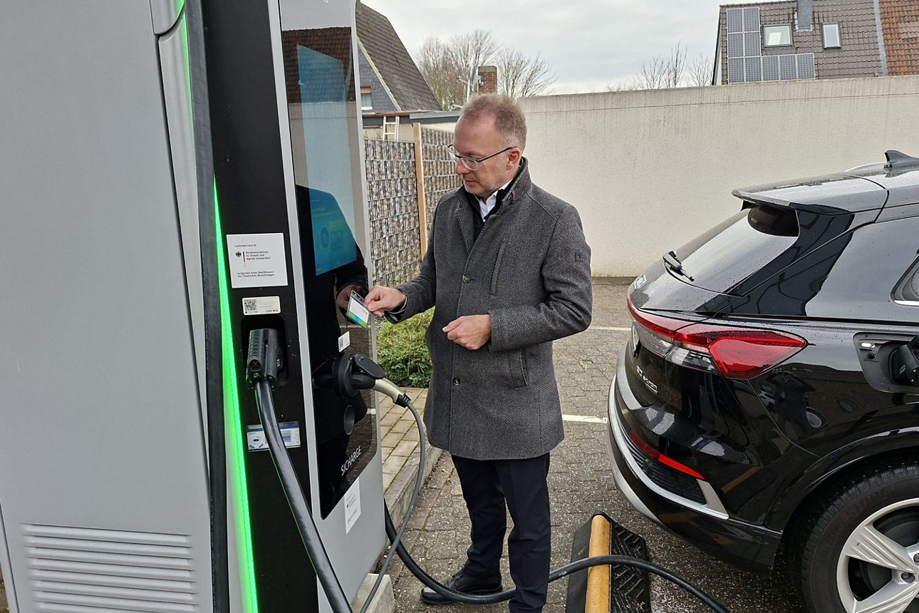 Nahaufnahme eines Elektroauto-Besitzers, der seine Zahlungskarte an eine moderne Ladestation hält