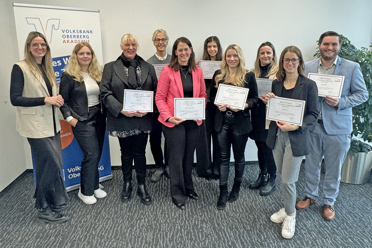 Gruppenfoto der erfolgreichen Absolventinnen und des Absolventen der Aufbauqualifizierung „Volksbank Oberberg Assistent“ mit ihren Zertifikaten, gemeinsam mit den Trainerinnen Lisa Dross und Mara Mischke in den Räumen der Volksbank Oberberg Akademie.