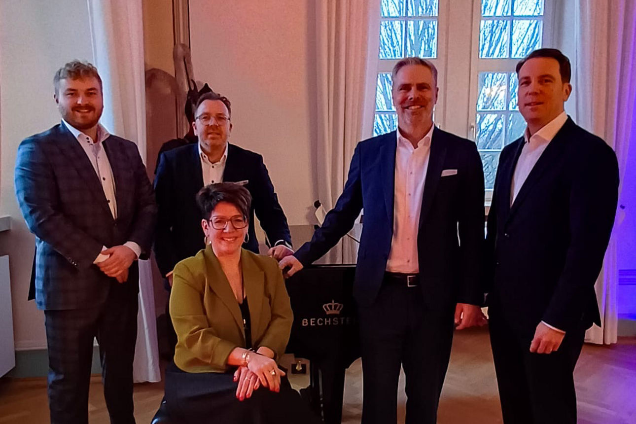 Eine Gruppe von Personen in formeller Kleidung in einem eleganten Raum mit großen Fenstern