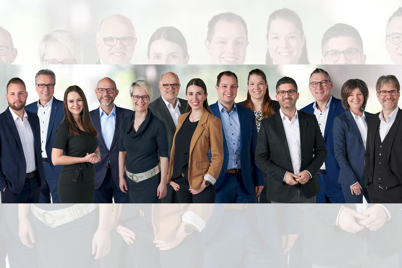 Eine Gruppe von Personen in formeller Kleidung steht zusammen vor einem neutralen Hintergrund.