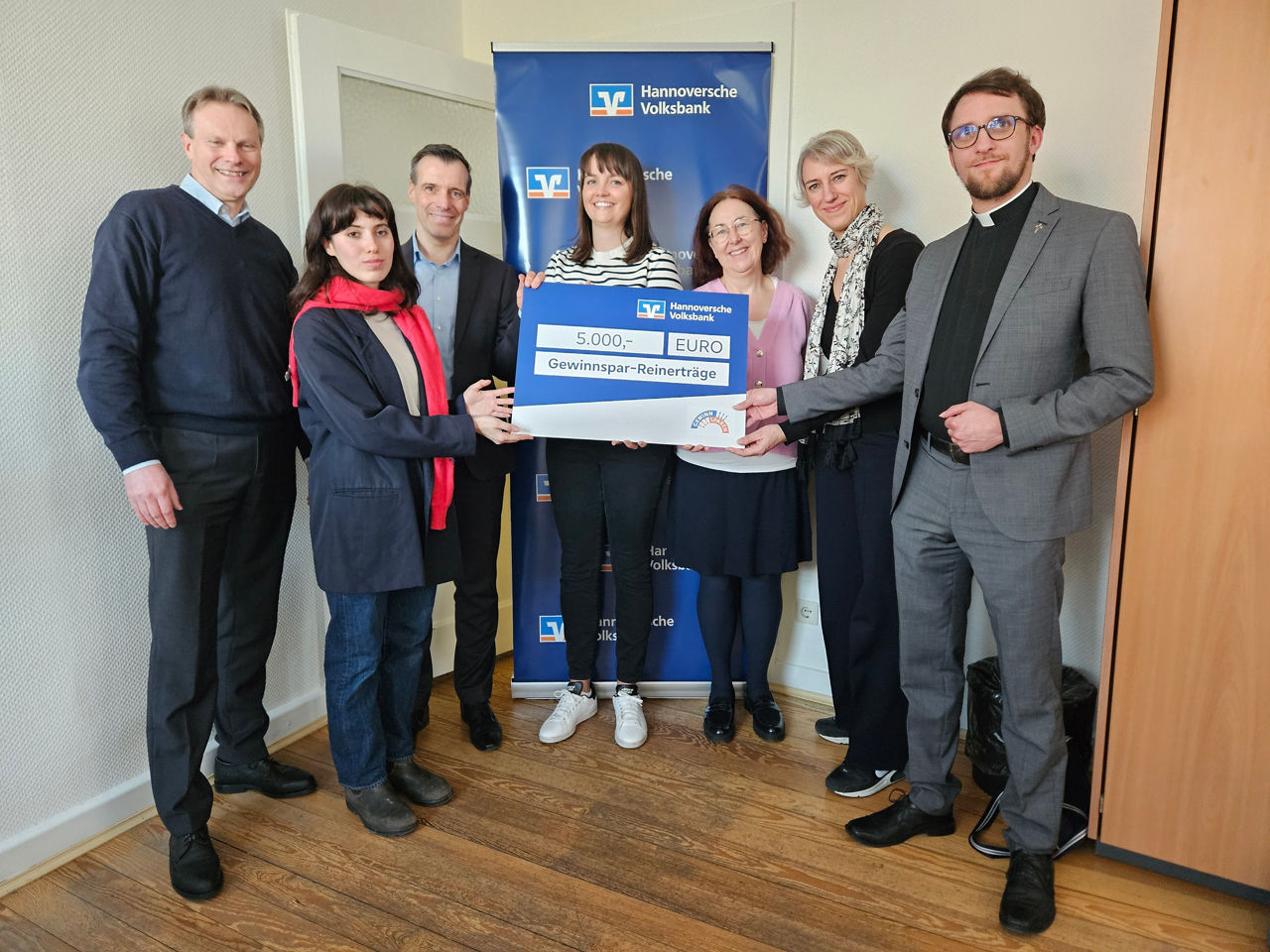 Sieben Personen halten ein Schild in der Hand, auf dem steht: "5.000 EURO Gewinnspar-Reinerträge