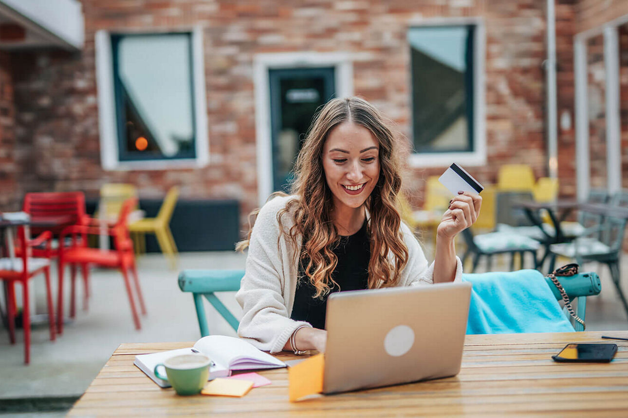Eine junge Frau sitz in einem Innenhof an ihrem Laptop und tippt eine Überweisung ein