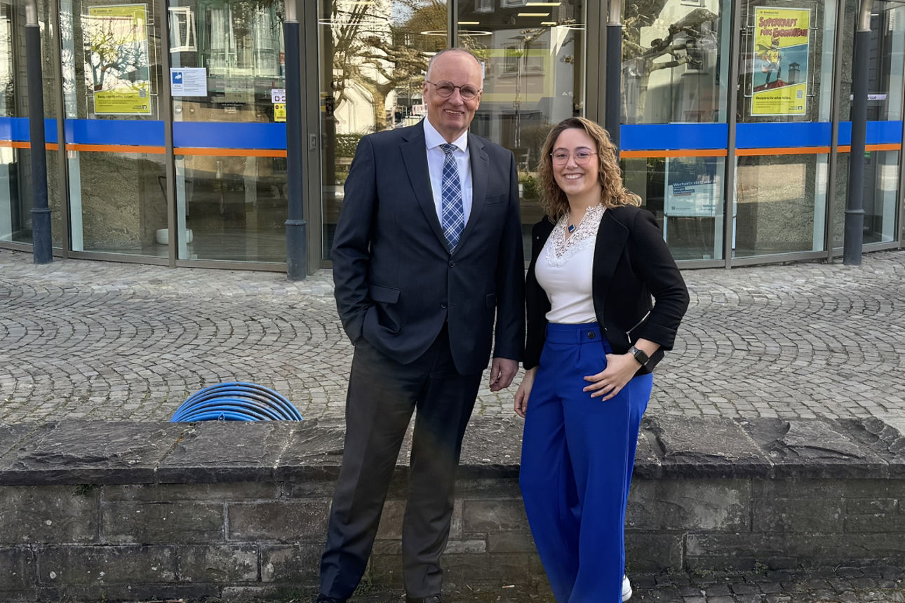 Niederlassungsleiter Stefan Weise und Geschäftsstellenleiterin Pia Wippenbeck stehen nebeneinander vor der Geschäftsstelle Engelskirchen und lächeln.