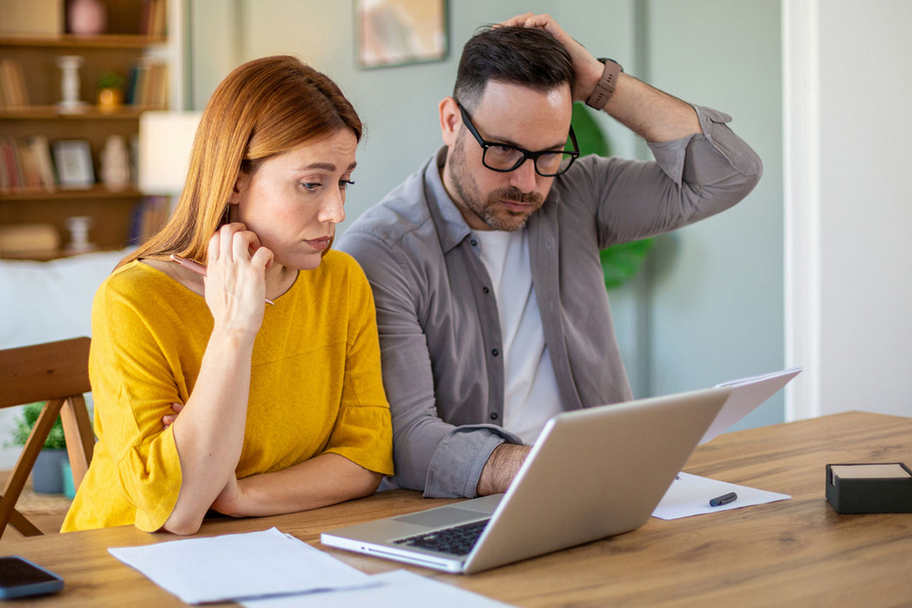 Pärchen sitzt am Tisch und schaut prüfend auf Laptop und Unterlagen
