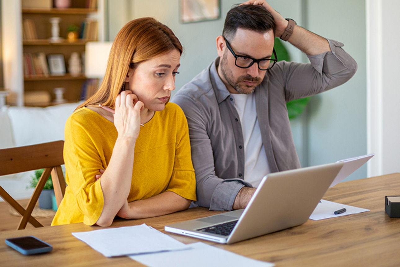 Pärchen sitzt am Tisch und schaut prüfend auf Laptop und Unterlagen