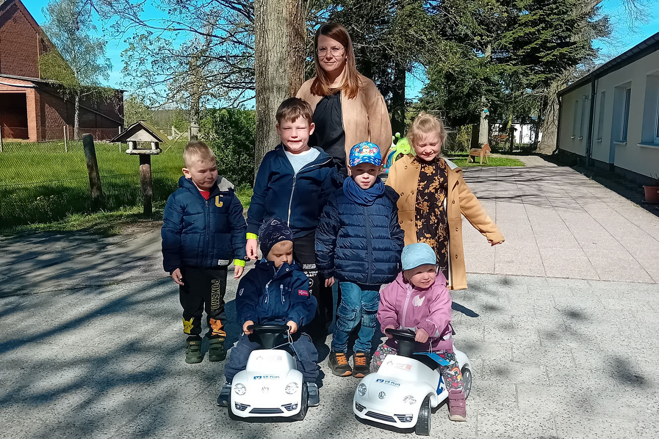 Sechs Kinderim freien mit zwei Bobbycars und einer Dame. 