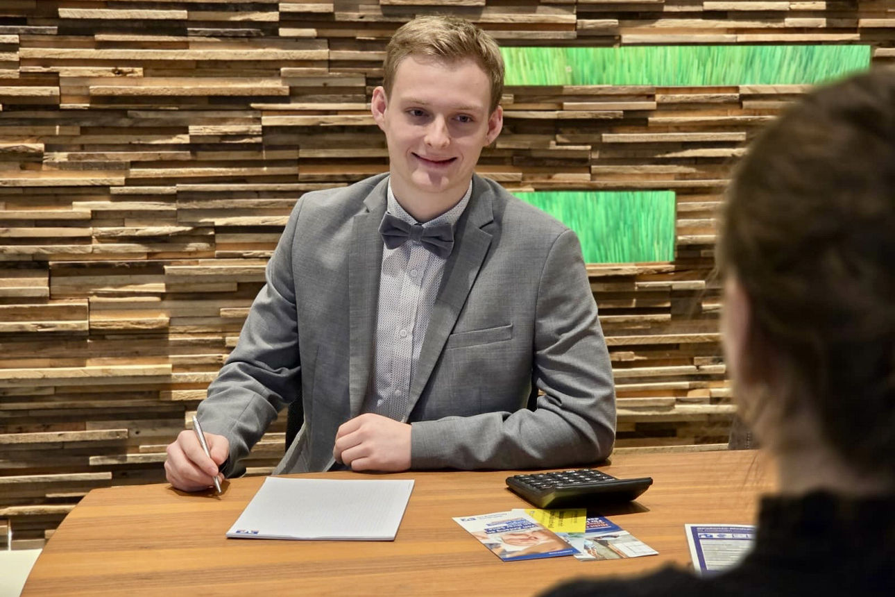 Luca Liesenberg sitzt in einer Geschäftsstelle der Volksbank Oberberg an einem Beratungstisch und führt ein Gespräch mit einer Kundin.