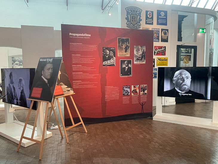 Blick in den Ausstellungsraum mit Infotafeln und Bildschirmen, auf denen Filmausschnitte gezeigt werden