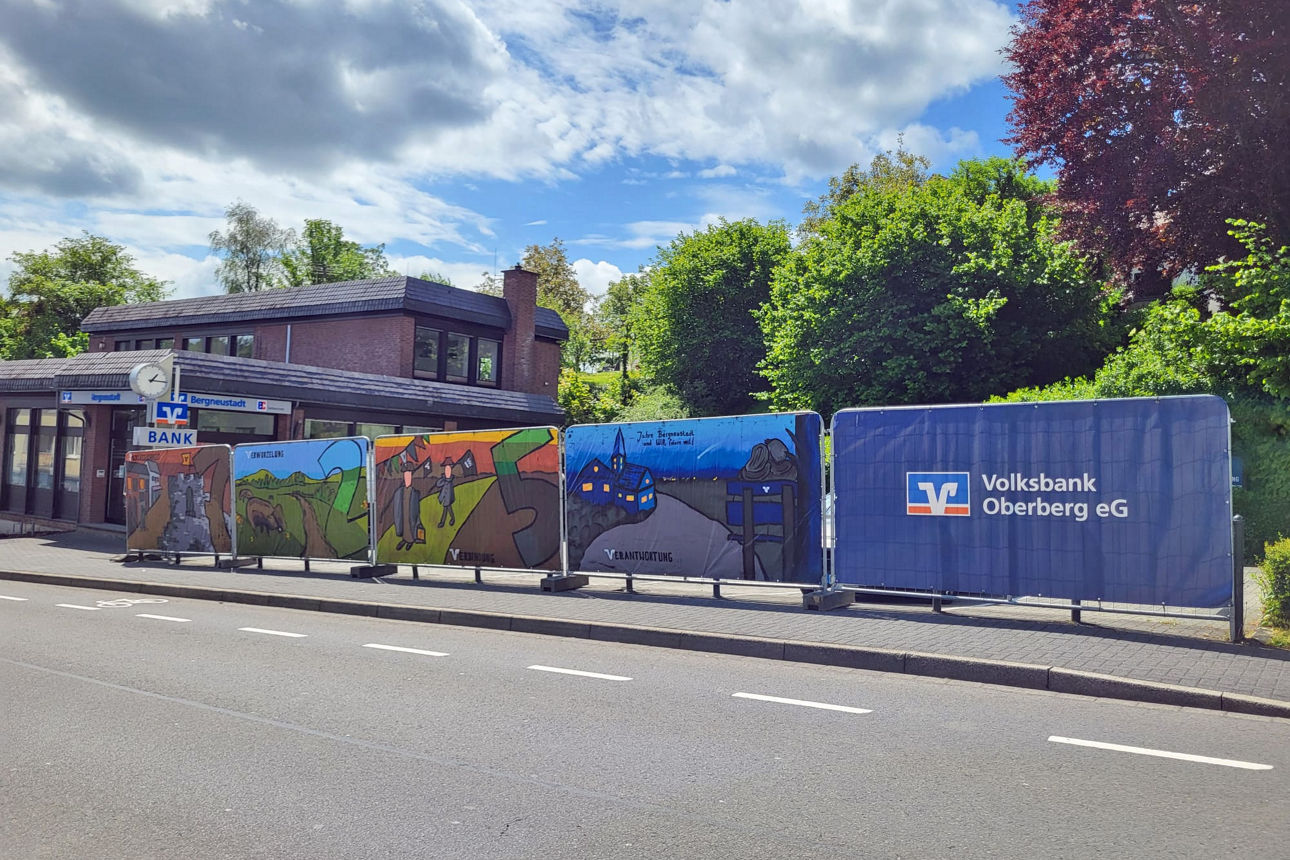 Großformatige Graffiti-Planen mit regionalen Motiven und Werten hängen an den Bauzäunen vor der Geschäftsstelle der Volksbank Oberberg in Bergneustadt, die aktuell modernisiert wird.