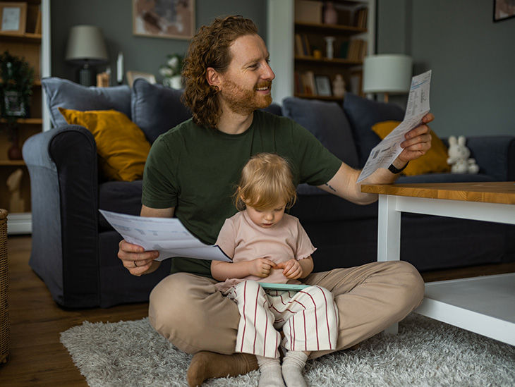 Tochter sitzt auf dem Schoß ihres Papas, der Unterlagen in der Hand hält