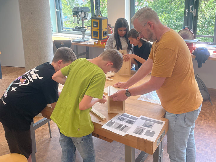 Schüler bauen mithilfe eines Erwachsenen einen Nistkasten für Vögel zusammen. 