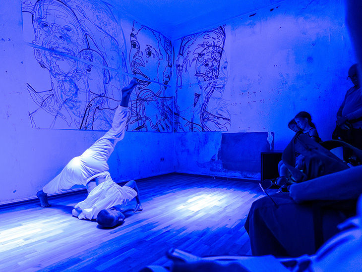 Ein Tänzer führt vor Zuschauern eine Choreografie auf. Der Raum ist mit blauem Licht ausgeleuchtet