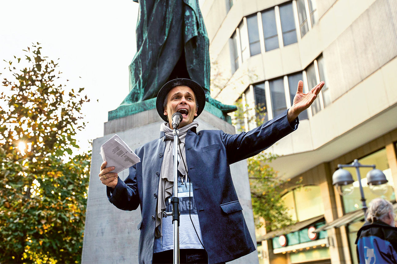 Ein Mann spricht leidenschaftlich in ein Mikrofon und hält Papiere in der Hand.