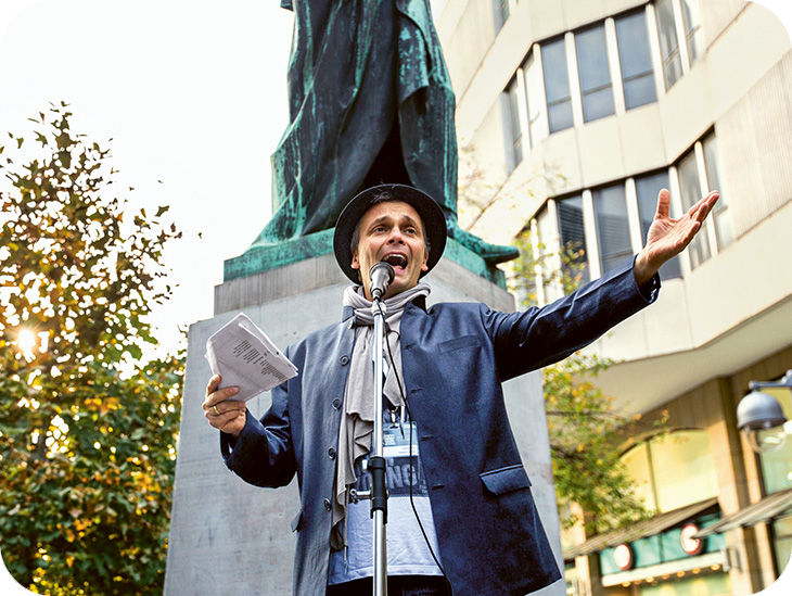 Ein Mann spricht leidenschaftlich in ein Mikrofon und hält Papiere in der Hand.