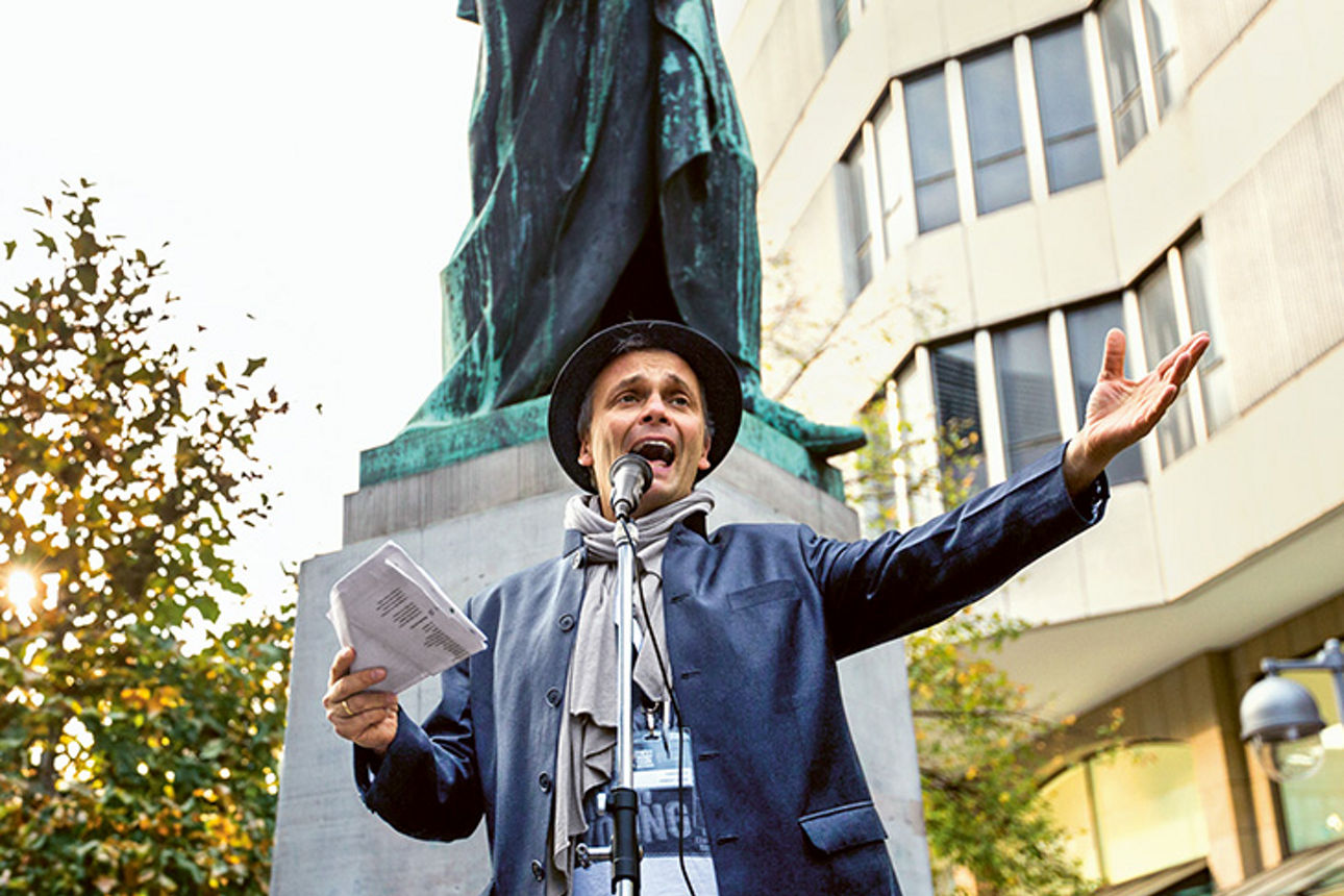 Ein Mann spricht leidenschaftlich in ein Mikrofon und hält Papiere in der Hand.
