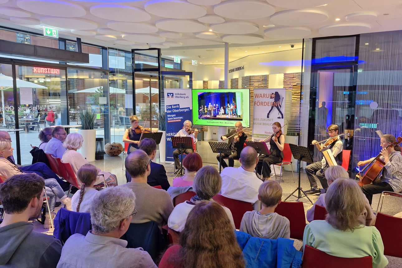 Konzertveranstaltung im Forum der Volksbank Oberberg: Mehrere Ensemblemitglieder spielen Geigen und Cello vor einem aufmerksam zuhörenden Publikum.