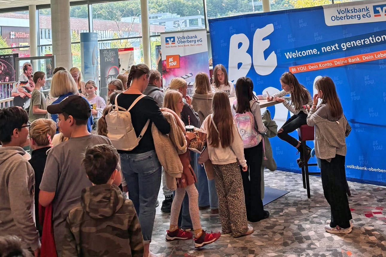 Bela und Charlotte Plass sitzen an einem Tisch im SEVEN Kinocenter Gummersbach und geben Autogramme. Vor ihnen wartet eine Schlange junger Kinogäste.