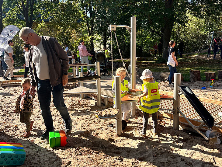 Kinder spielen auf einer Sandbaustelle. Sie sind dort teils mit ihren Eltern. 