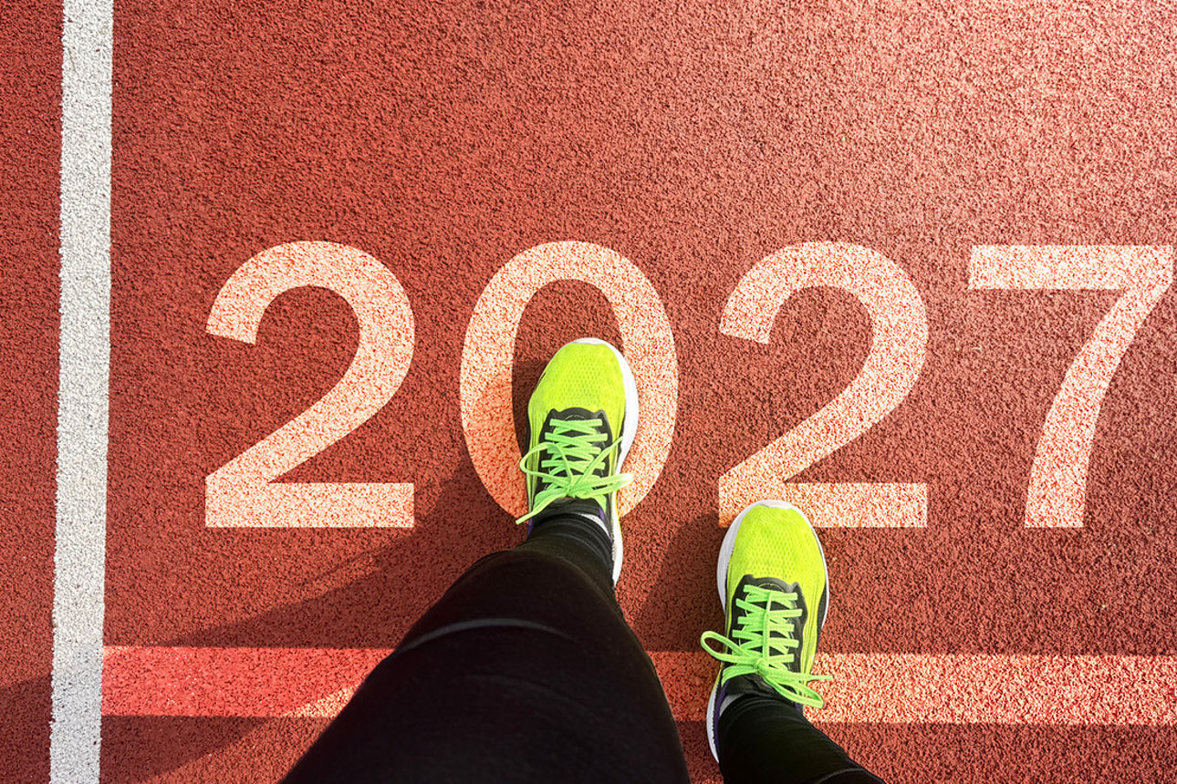 Ein Läufer mit neongelben Sportschuhen steht auf einer Startlinie mit der Zahl „2027“.