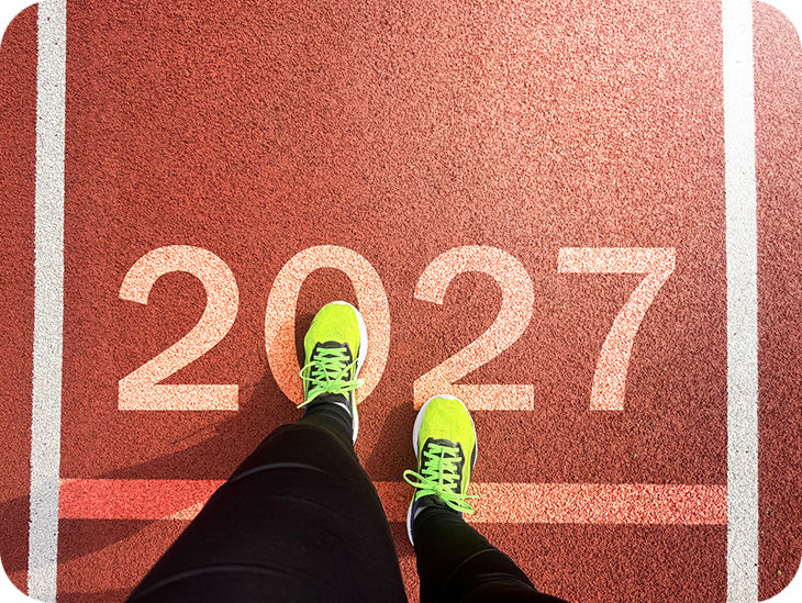 Ein Läufer mit neongelben Sportschuhen steht auf einer Startlinie mit der Zahl „2027“.