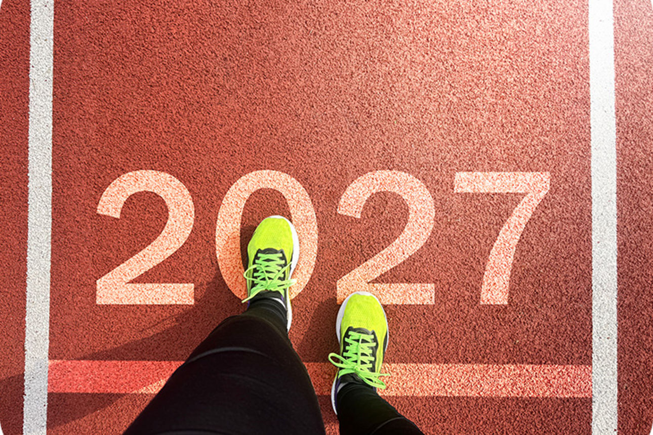 Ein Läufer mit neongelben Sportschuhen steht auf einer Startlinie mit der Zahl „2027“.