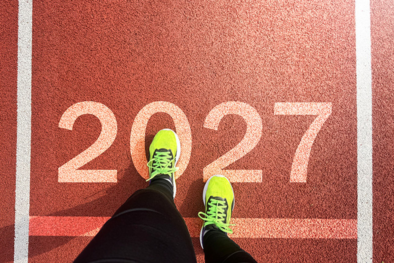 Ein Läufer mit neongelben Sportschuhen steht auf einer Startlinie mit der Zahl „2027“.