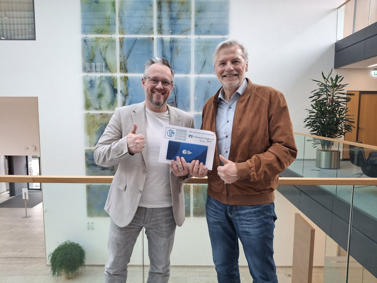 Zwei Männer stehen zusammen vor einem großen Fenster, wobei natürliches Licht ihre Umgebung erhellt
