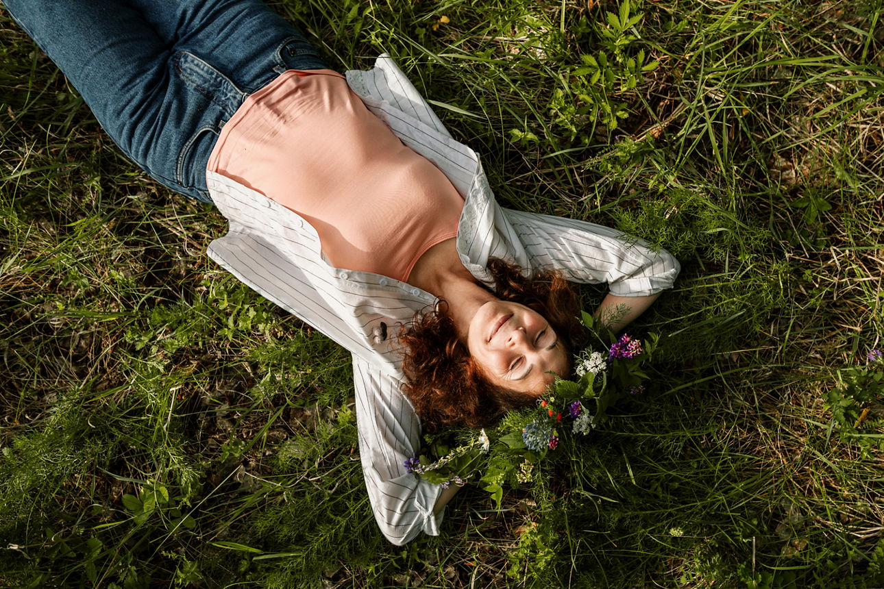 Eine Frau liegt auf einer Blumenwiese in der Sonne und lacht
