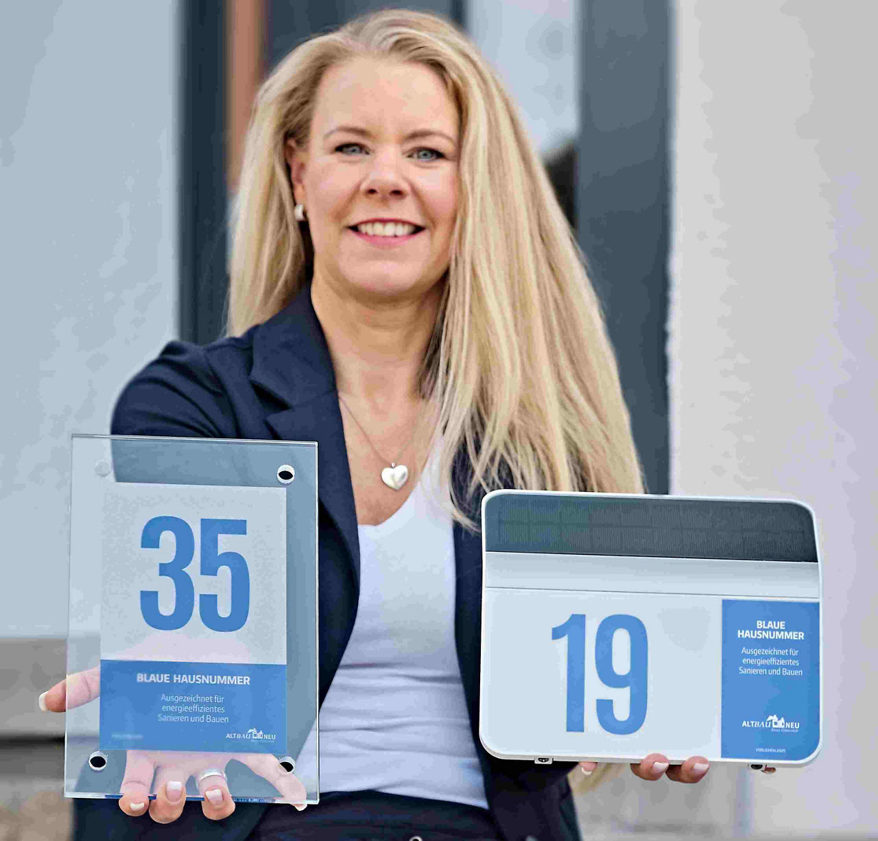 Junge Frau mit Solarleuchten und Glasschild des Wettbewerbs "Blaue Hausnummer"
