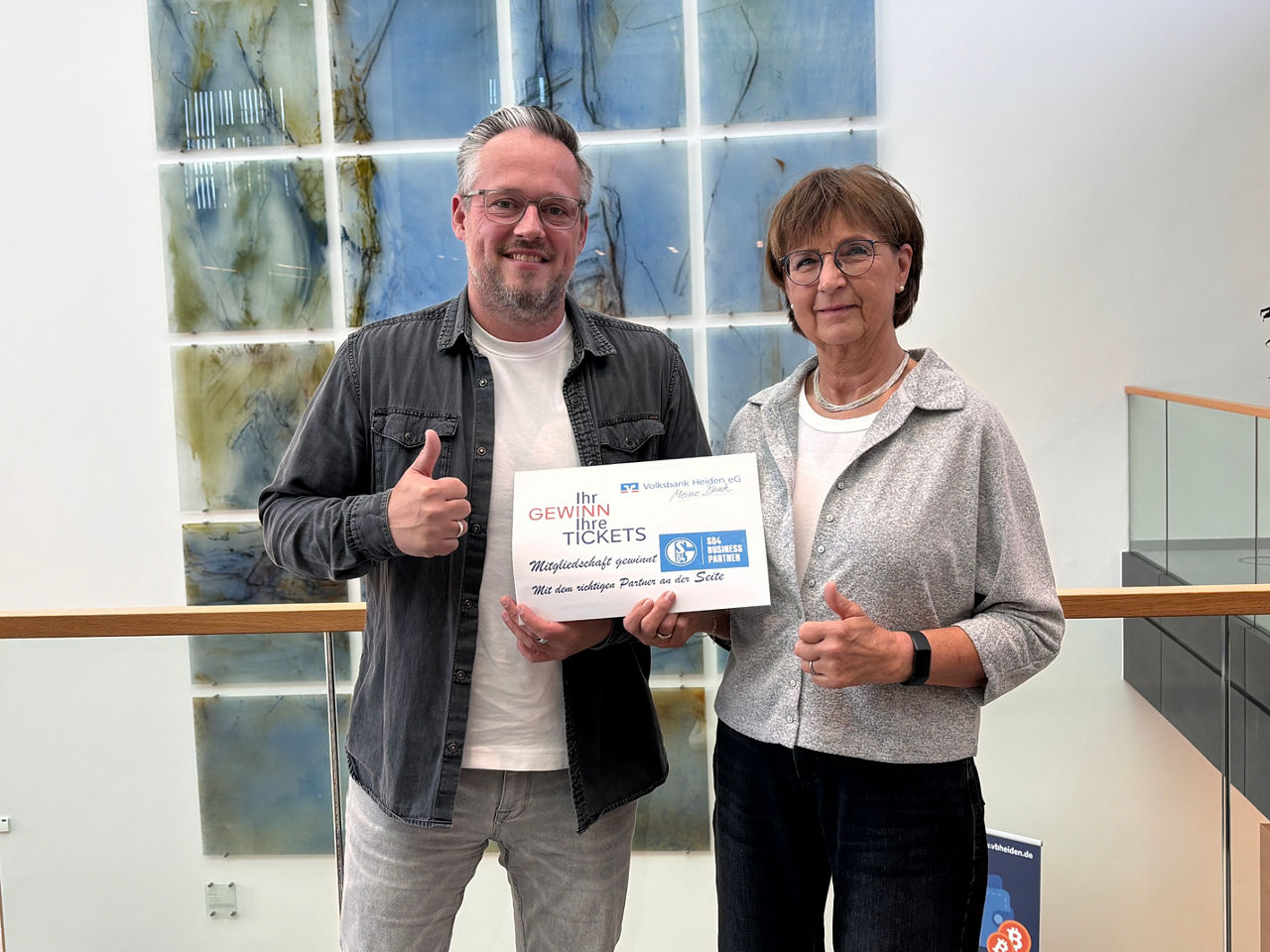 Ein Mann und eine Frau präsentieren gemeinsam einen Gewinn-Gutschein für FC Schalke 04 Tickets.
