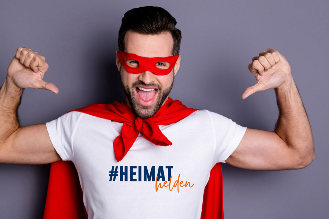 Junger Mann mit rotem Umhang zeigt mit beiden Daumen auf sich.