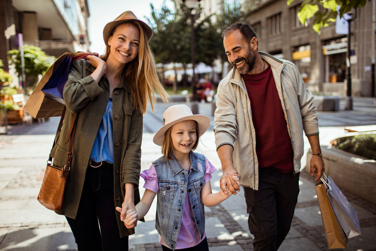 Familie mit einem Mädchen geht entspannt eine Straße beim Shoppen entlang.