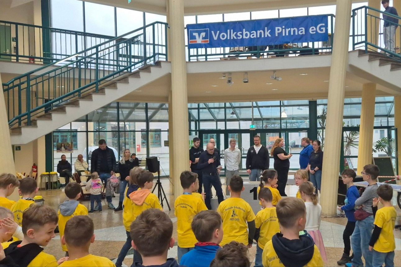 Eröffnung der Veranstaltung, Erwacshene stehen auf der Bühne und sprechen zu Kindern, die von hinten sichtbar sind