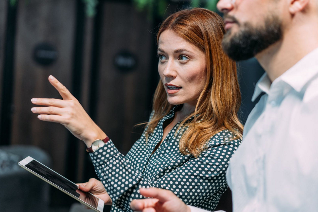 Geschäftsfrau zeigt erklärend auf einen nicht zu sehenden Gegenstand.